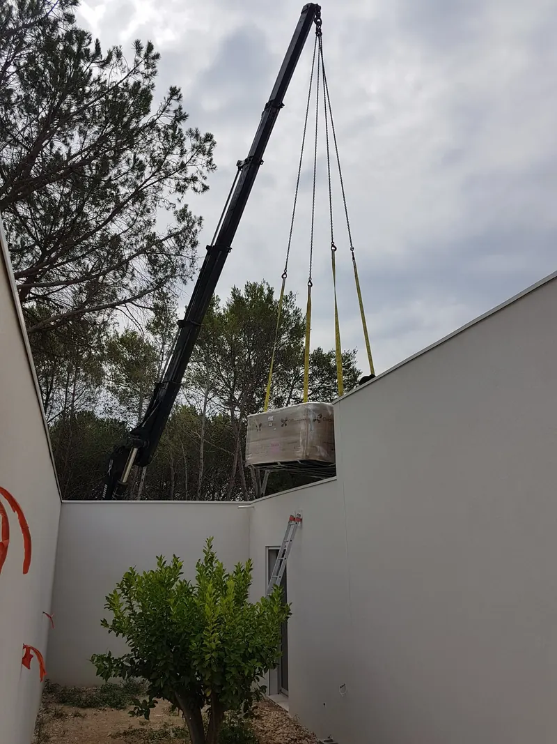 La grue fait passer le spa par-dessus le mur d'une cour étroite à Langlade