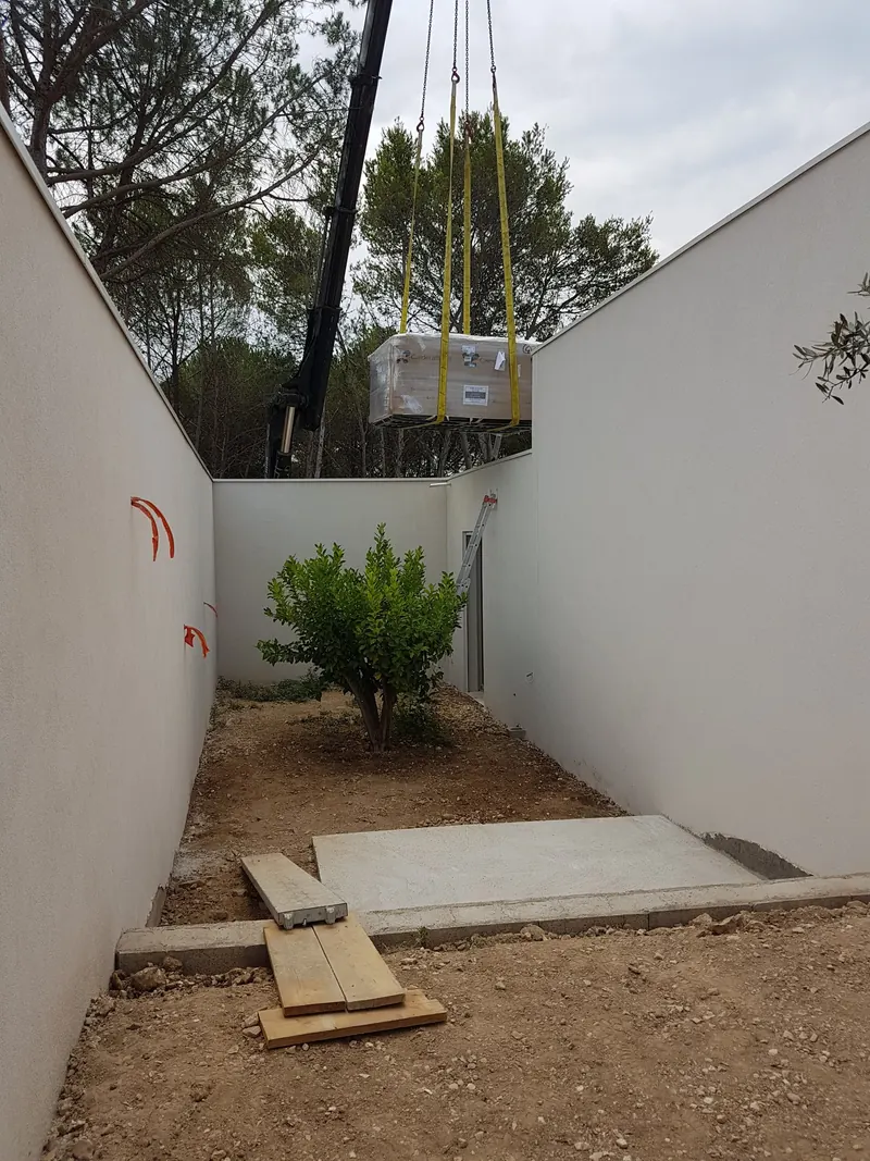 Spa Caldera descendu à la grue vers une dalle béton, dans une cour entre murs blancs, à Langlade