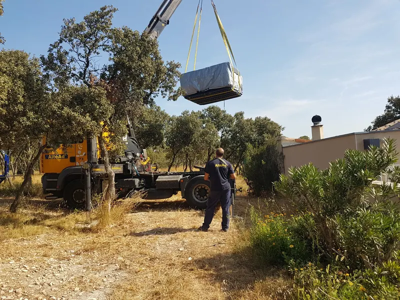 Spa bâché levé par la grue d'un camion au milieu des chênes, opérateur de dos, aux Angles