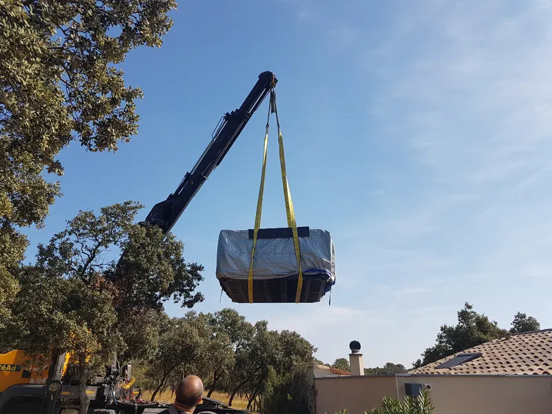 Spa sous bâche suspendu à la flèche d'une grue, haut dans le ciel au-dessus des arbres, aux Angles