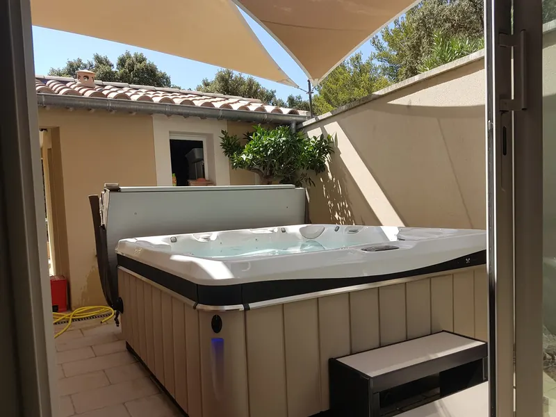 Spa installé dans un patio clos sous deux voiles d'ombrage, vu depuis la baie vitrée, aux Angles