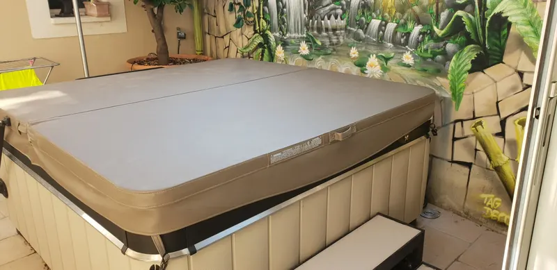 Spa fermé par sa couverture taupe, avec marchepied, dans une cour au mur peint aux Angles