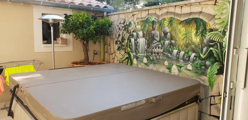 Spa couvert dans une petite cour, devant un mur peint d'une fresque de cascade, aux Angles