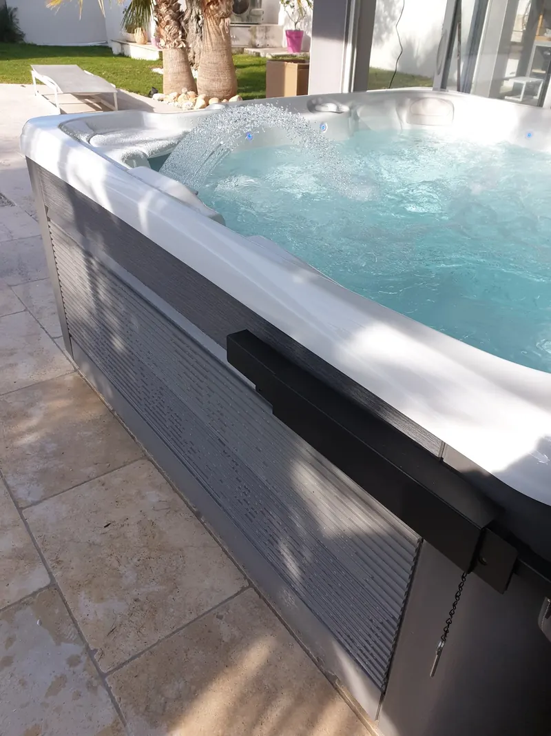 Spa Caldera en eau avec sa cascade, lève-couverture sur le flanc, jardin et palmiers derrière, à Vic-la-Gardiole