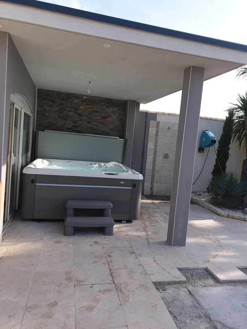 Terrasse couverte avec le spa au fond, pilier, douche extérieure et dallage en finition, à Vic-la-Gardiole