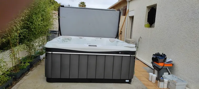 Spa blanc Caldera rempli d'eau turquoise, sur une terrasse en bois, piscine visible à côté