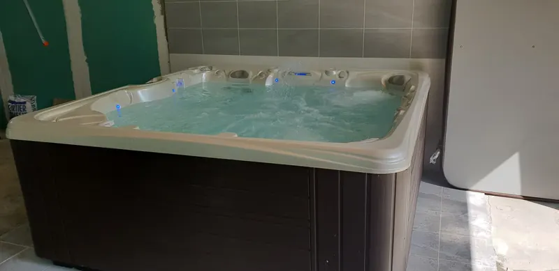 Spa à habillage brun foncé contre un mur carrelé gris, couverture dressée à côté, à Canohès