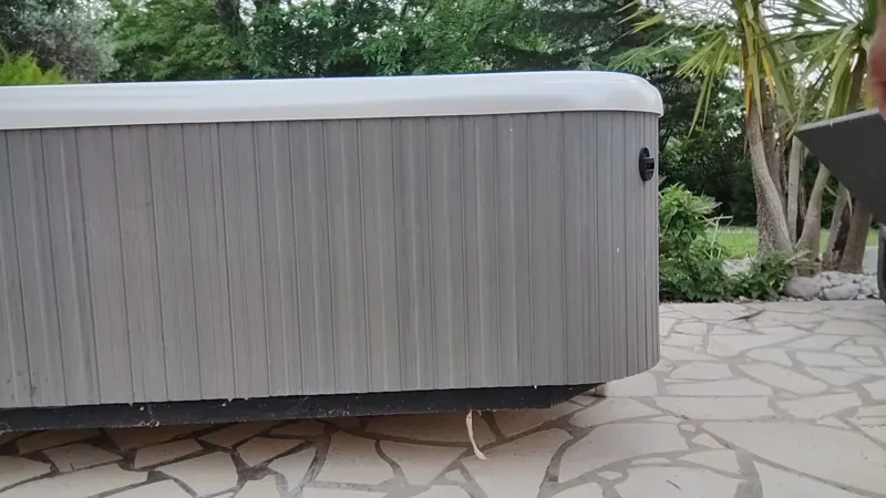Spa à habillage gris couché sur la terrasse en dalles de pierre, palmiers derrière