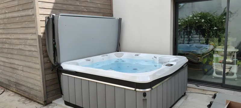 Spa blanc et bleu dans un coin étroit, entre des murs de pierre, sur une dalle