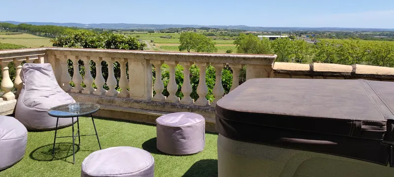 Terrasse en gazon : fauteuil-pouf, table en verre et poufs à côté du spa couvert