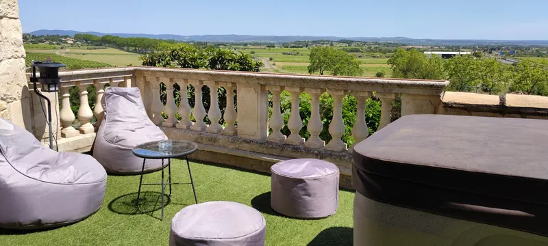 Vue élargie de la terrasse, poufs et table devant la balustrade, spa couvert à droite
