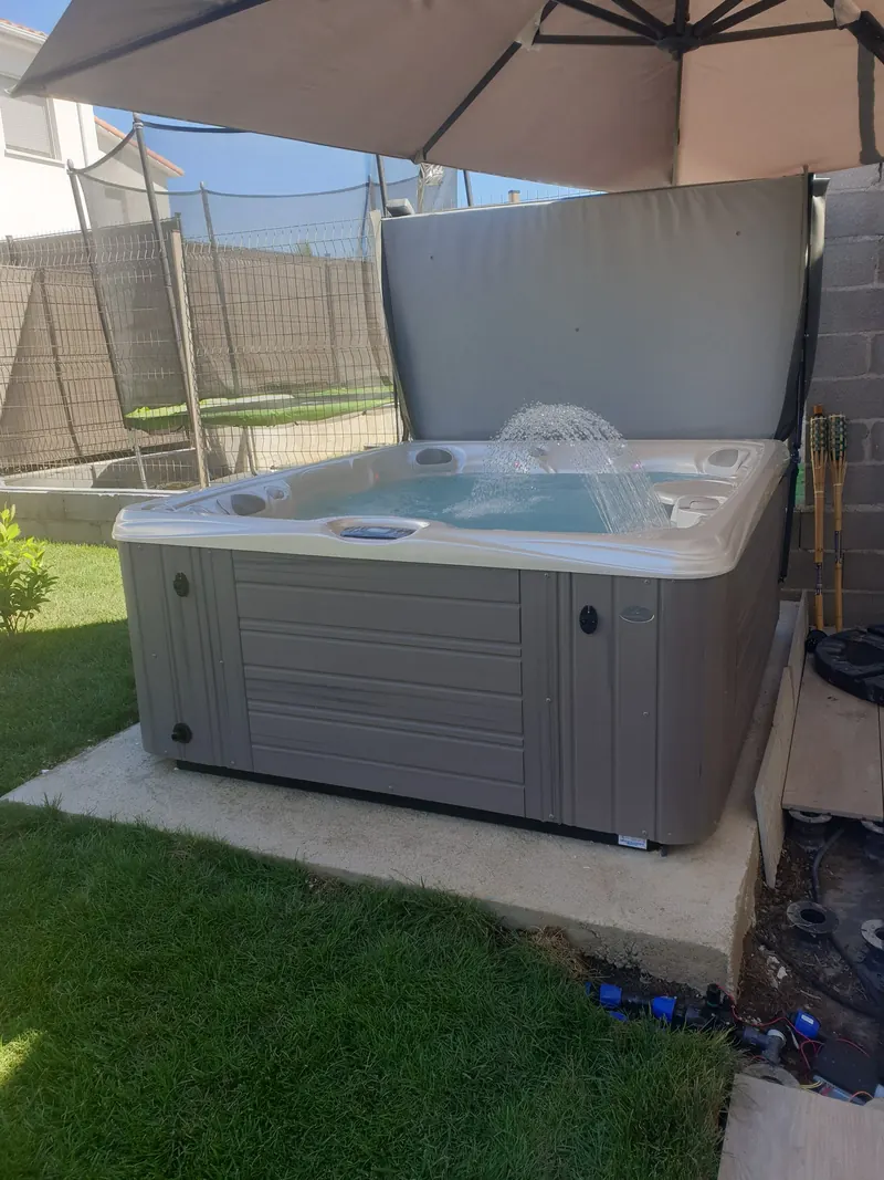 Spa gris rempli, fontaine en marche, posé sur une dalle béton dans un jardin à Cournonterral