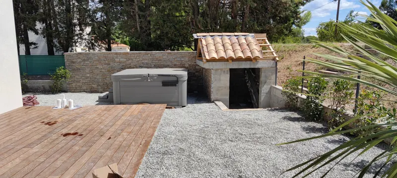 Spa gris et blanc sur la terrasse en bois, avec un mur de pierre et une pergola