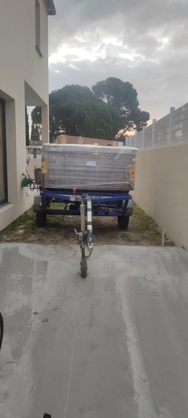 Spa blanc porté par un chariot bleu dans une ruelle étroite, entre deux murs