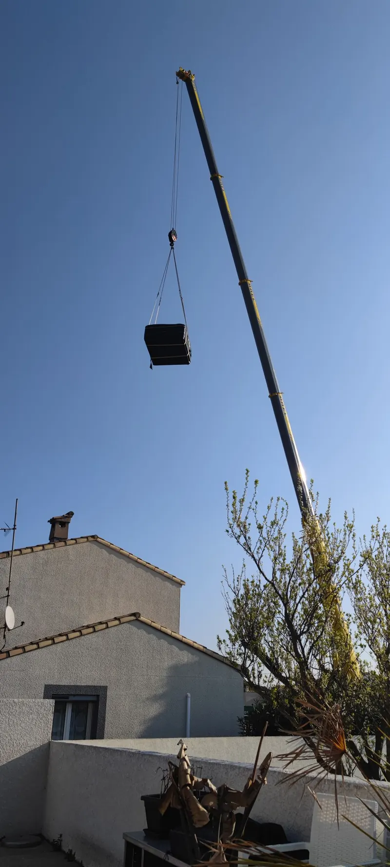Spa emballé de noir suspendu au crochet d'une grue, au-dessus des toits d'un quartier résidentiel