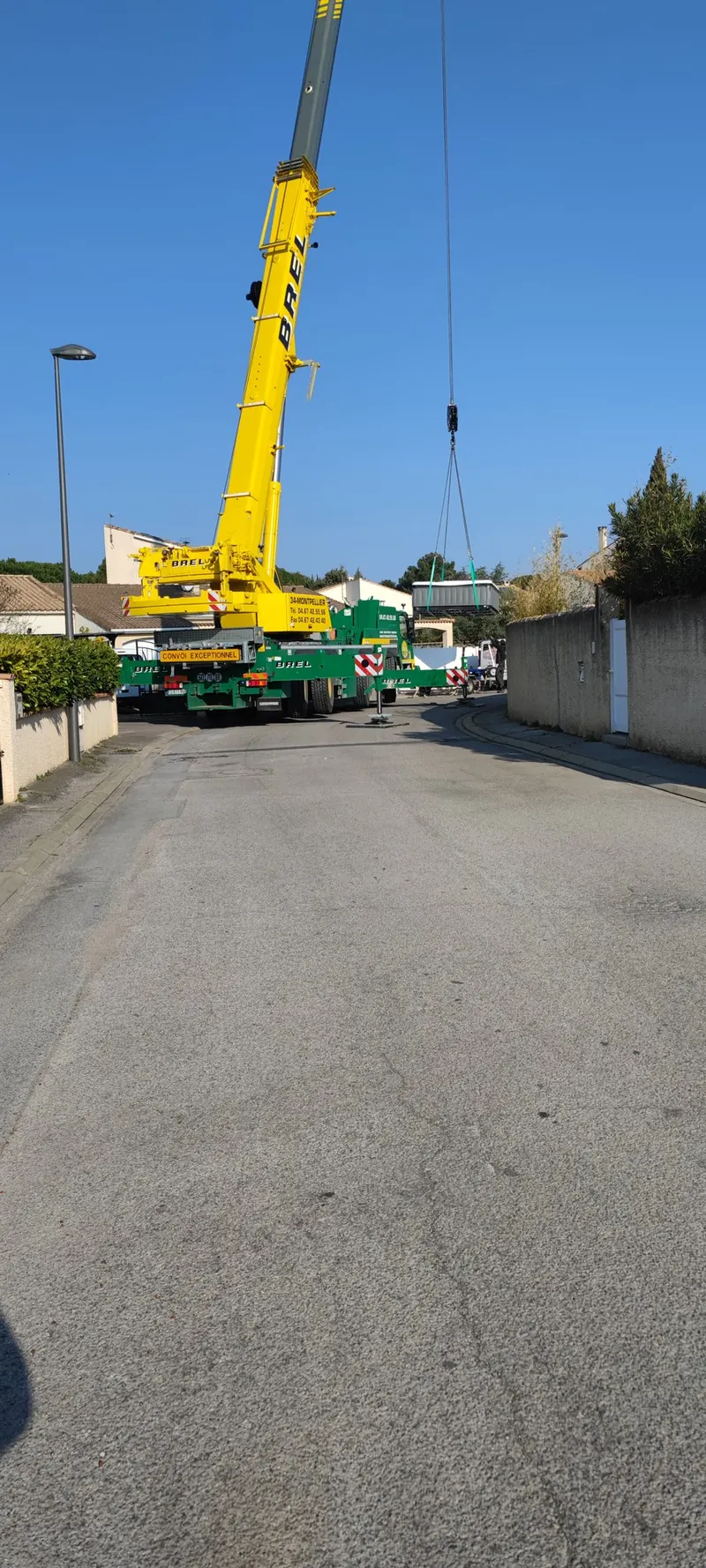 Grue mobile jaune et verte en pleine rue, spa suspendu au bout du câble