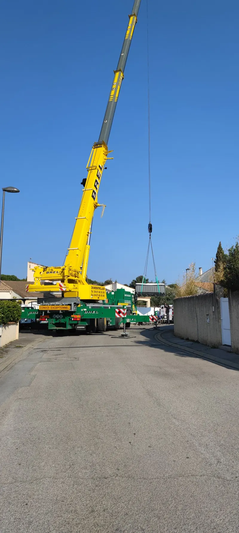 Grue mobile stabilisée dans la rue, spa en l'air au-dessus des clôtures