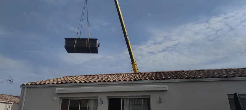 Spa noir emballé soulevé par la grue au-dessus du faîte d'une maison à tuiles