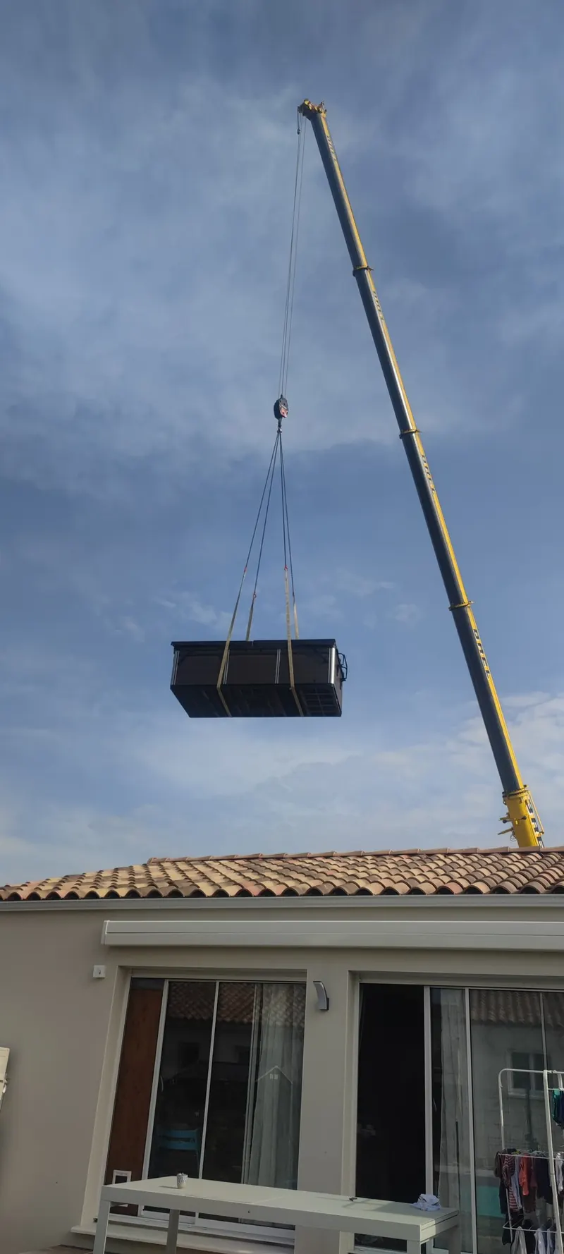 Grue en position finale, spa noir emballé suspendu, maison en arrière-plan