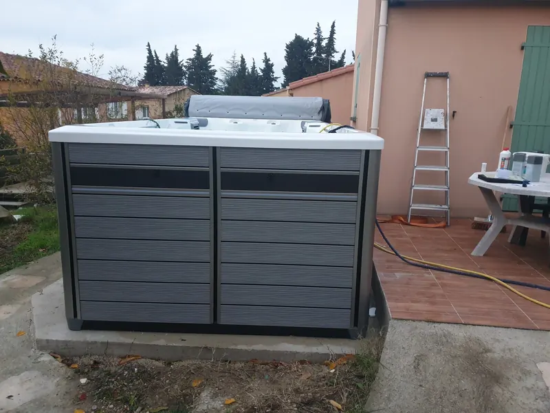 Spa de nage à habillage gris posé sur une dalle béton au pied d'une maison à Bollène