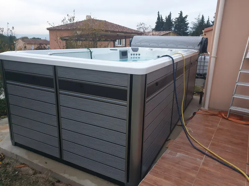 Spa de nage en cours de remplissage, deux tuyaux plongés dans le bassin, près d'une terrasse carrelée