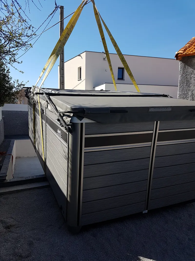 Spa de nage posé au sol, encore sanglé, à côté de la fosse prévue pour l'encastrer