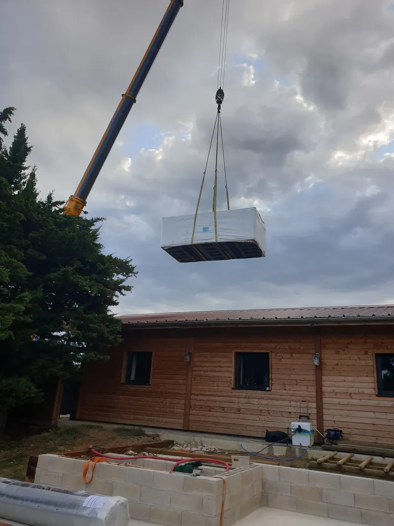 Spa de nage emballé suspendu à la grue au-dessus d'une maison en bois à Narbonne