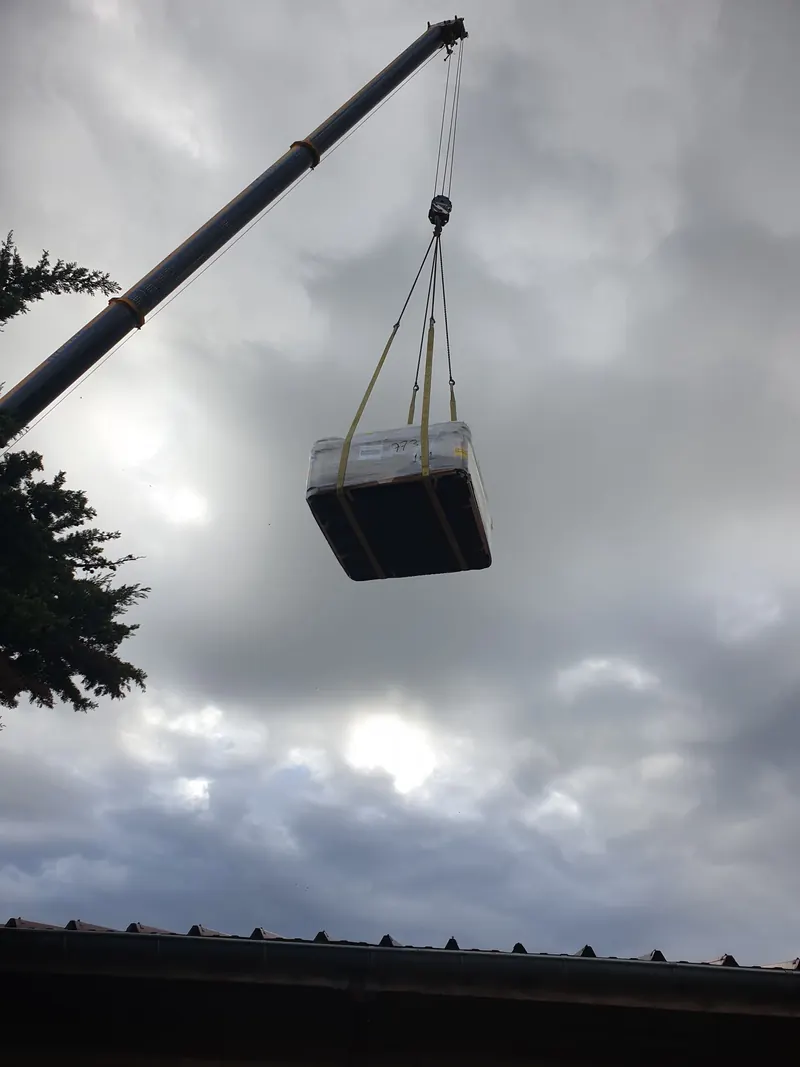 Spa emballé suspendu à la flèche d'une grue sous un ciel nuageux à Narbonne