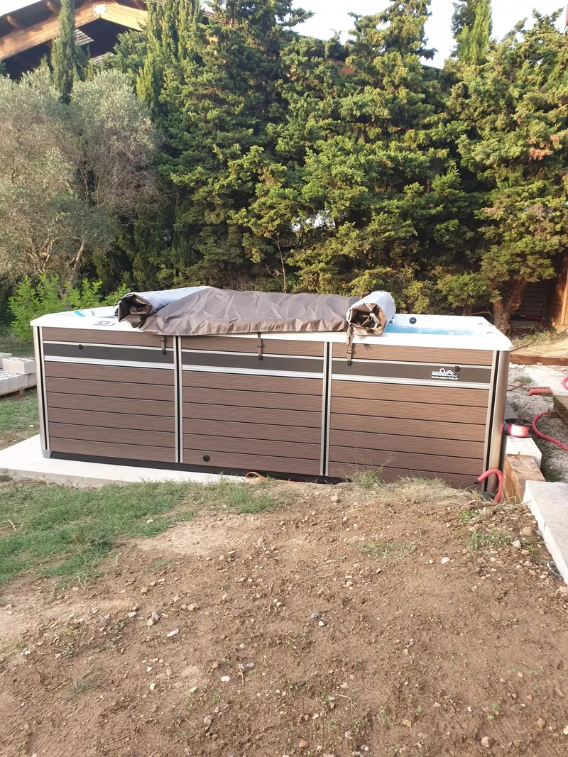 Spa de nage Endless Pools habillé de panneaux bruns, posé sur une dalle dans un jardin à Narbonne