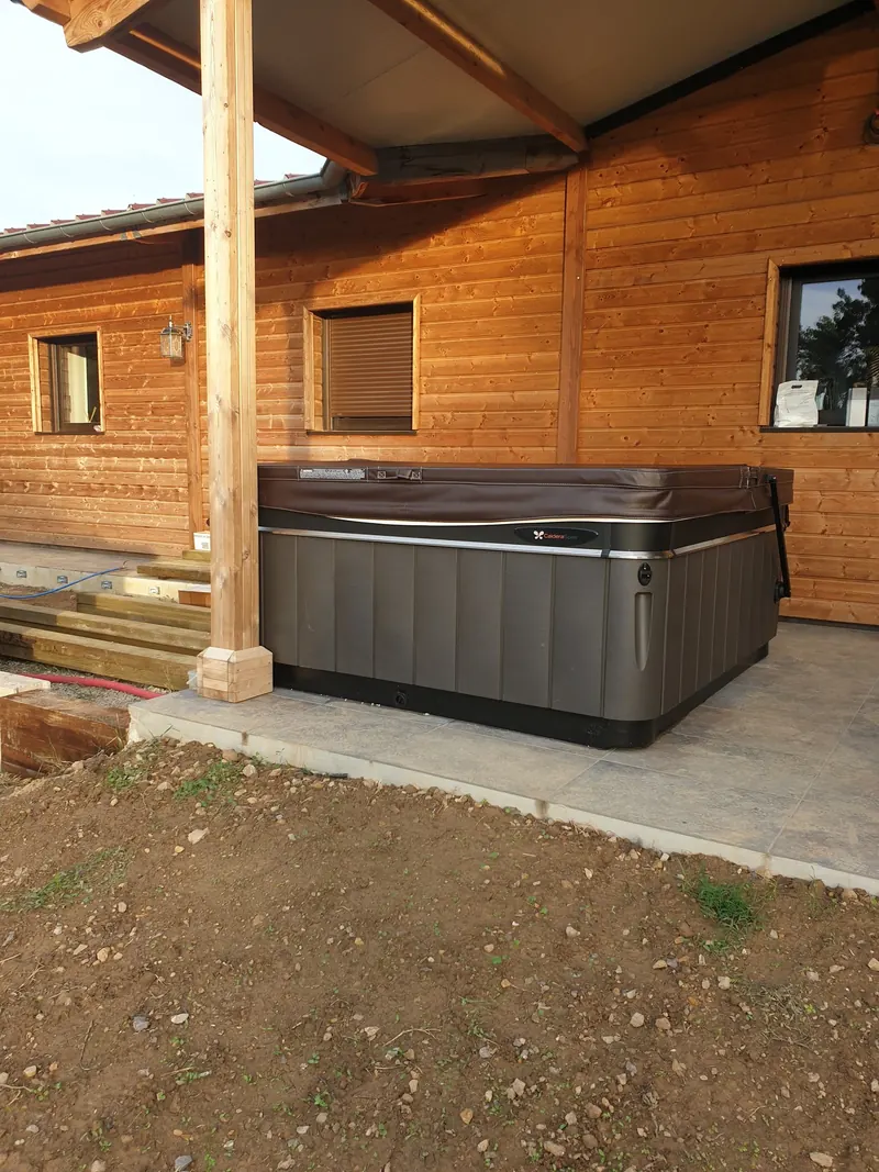 Spa Caldera gris foncé, couvercle fermé, posé sous l'avant-toit d'une maison en bois à Narbonne