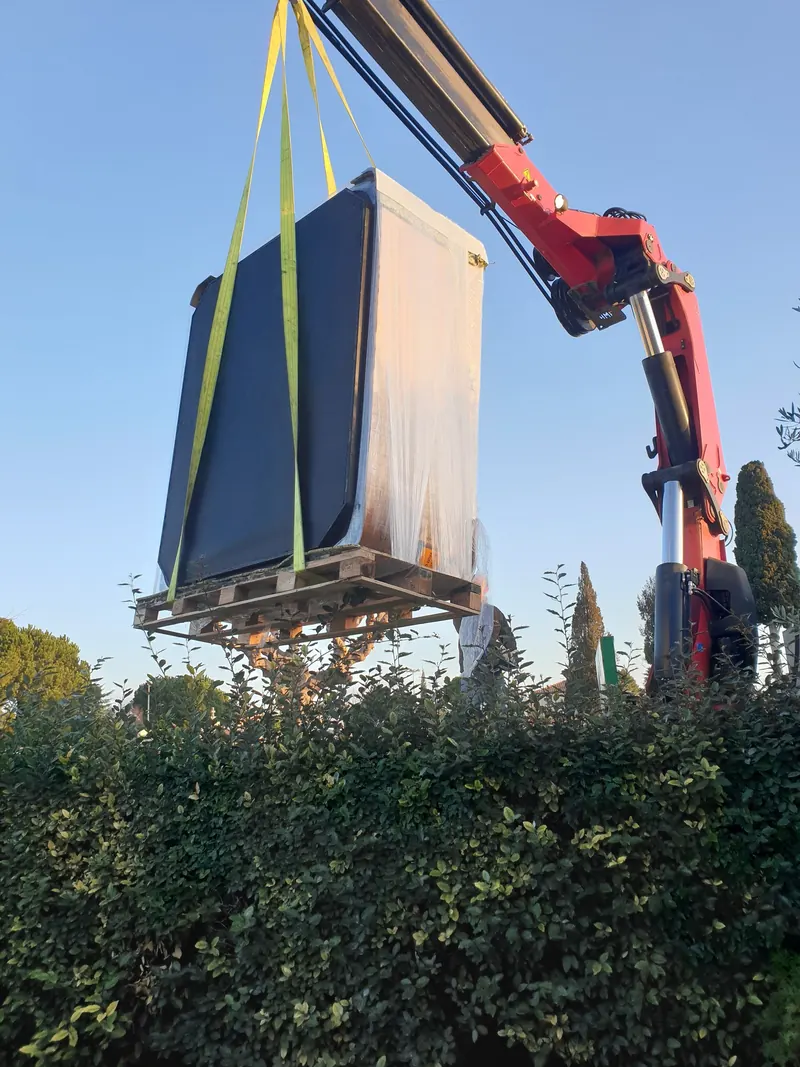 Spa emballé sur sa palette, suspendu à une grue rouge au-dessus d'une haute haie à Fabrègues