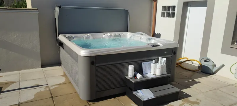 Spa gris à couverture relevée, jet d'eau en arc, marches avec flacons et notices