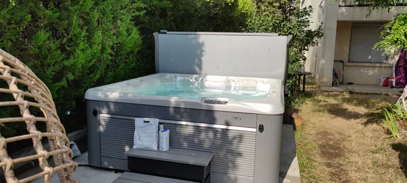 Spa blanc rempli d'eau turquoise, jets visibles, entouré de haies