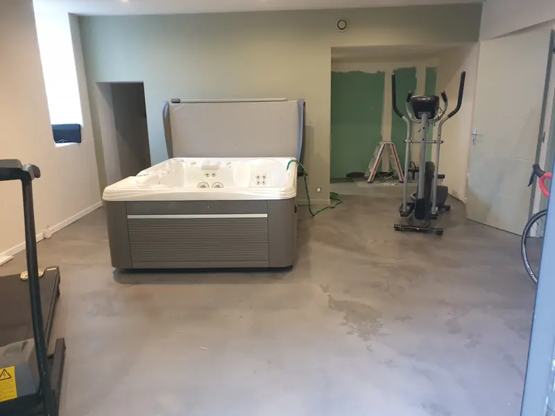 Spa posé dans une pièce au sol béton, entre un tapis de course et un vélo elliptique, à Gigean