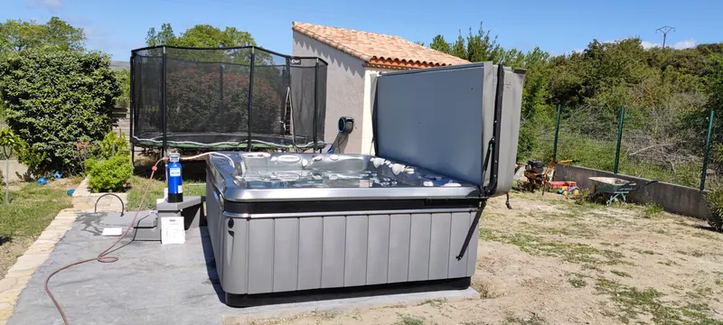 Spa gris ouvert dans le jardin, petit bâtiment à toit de tuiles au fond