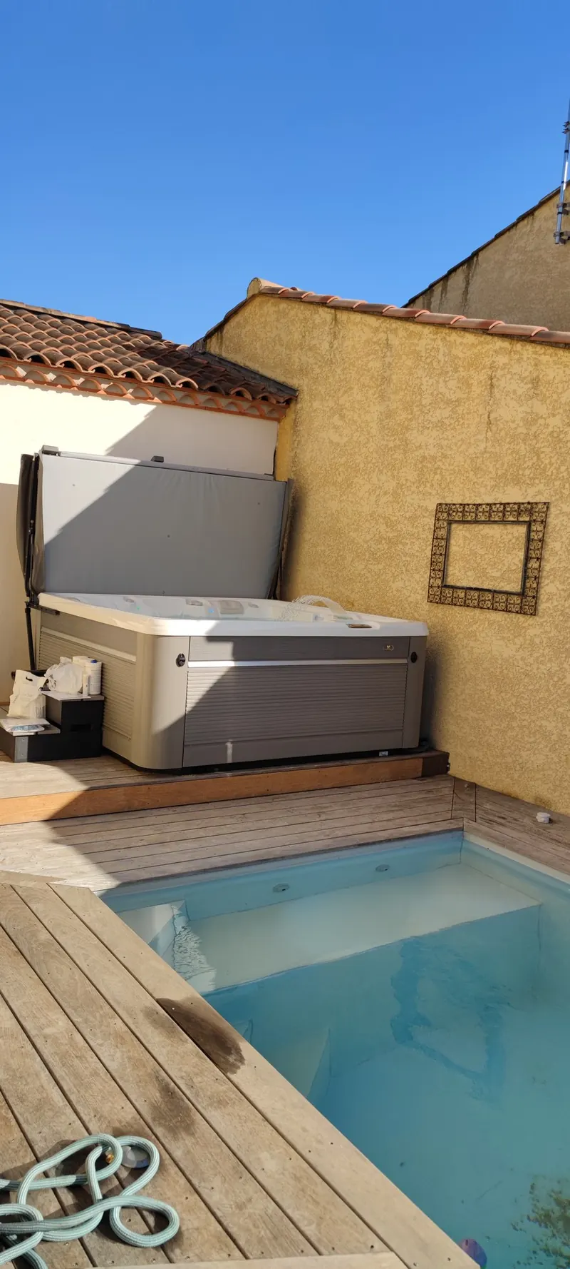Spa posé sur une terrasse en bois au bord d'un petit bassin, dans une cour