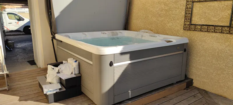Spa rempli sur sa terrasse en bois, contre le mur de la cour