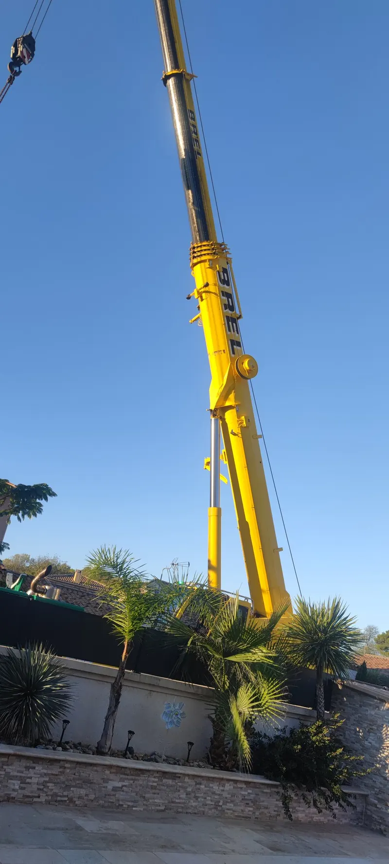 Levage du spa par une grue jaune, avec la maison blanche et la piscine bleu turquoise