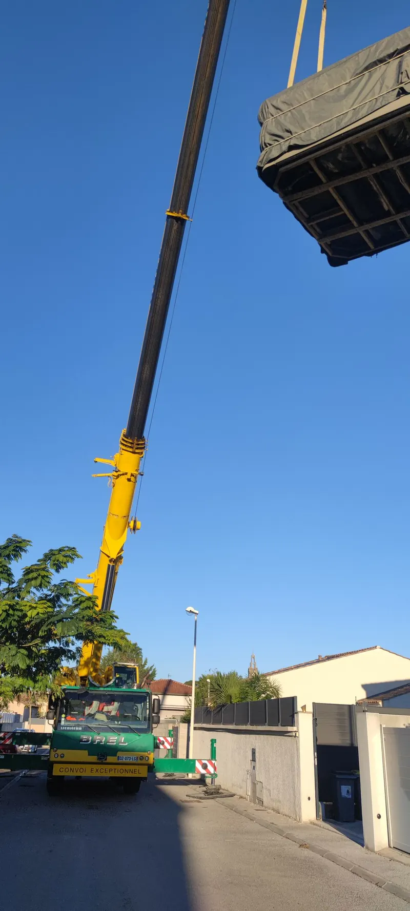 Levage du spa, avec la grue jaune déployée, la maison et la route d'accès