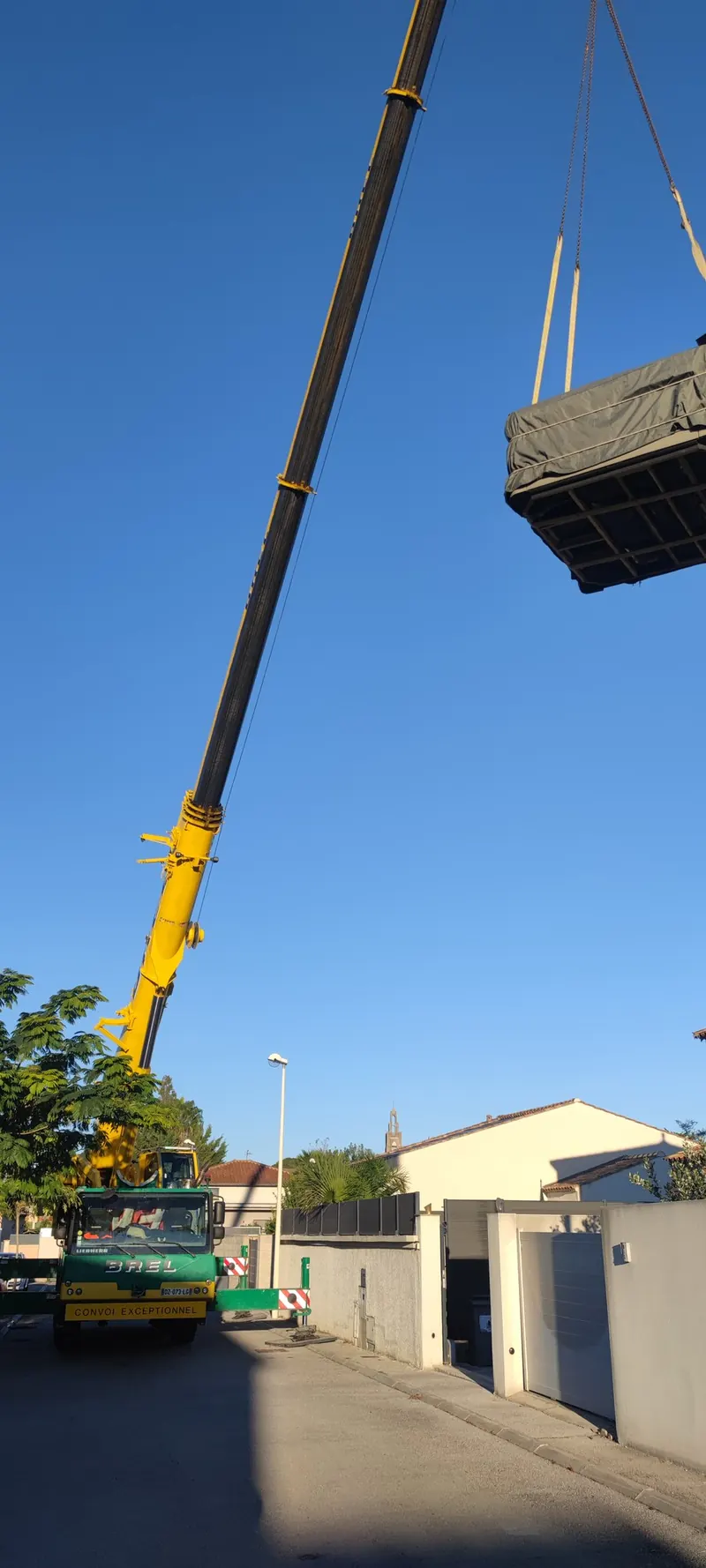 Grue jaune avec le spa en caisson suspendu, maison et terrain en arrière-plan