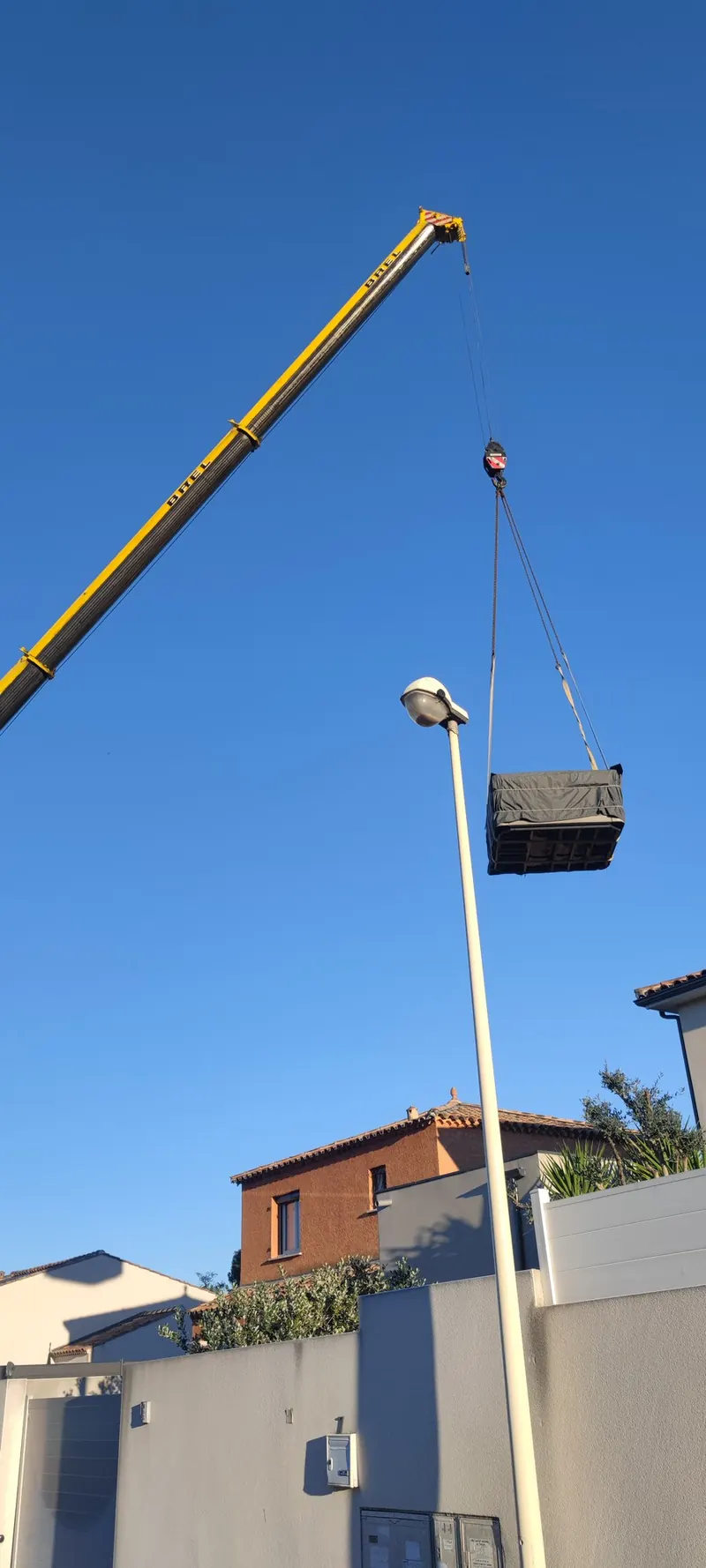 Spa levé à sa hauteur maximale, grue jaune déployée, ciel dégagé et bâtiments anciens visibles
