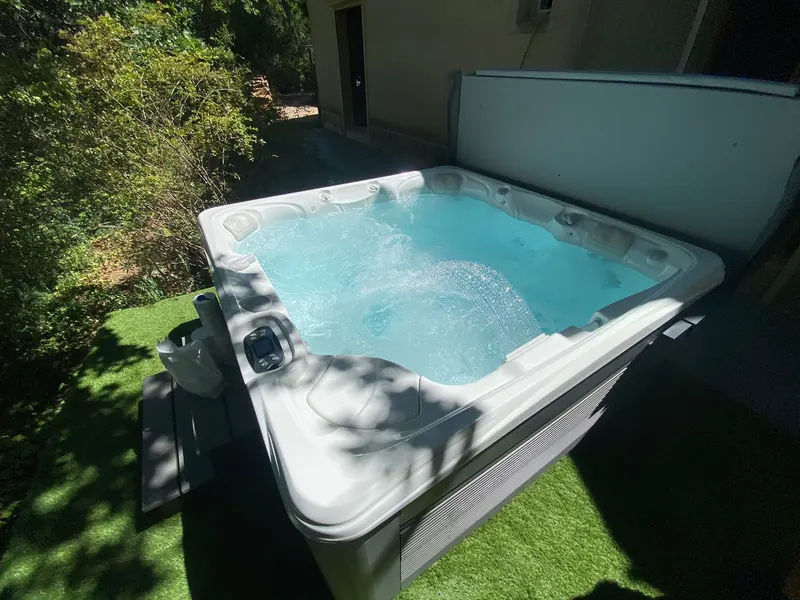 Spa blanc dans une pièce couverte carrelée, avec le jardin visible