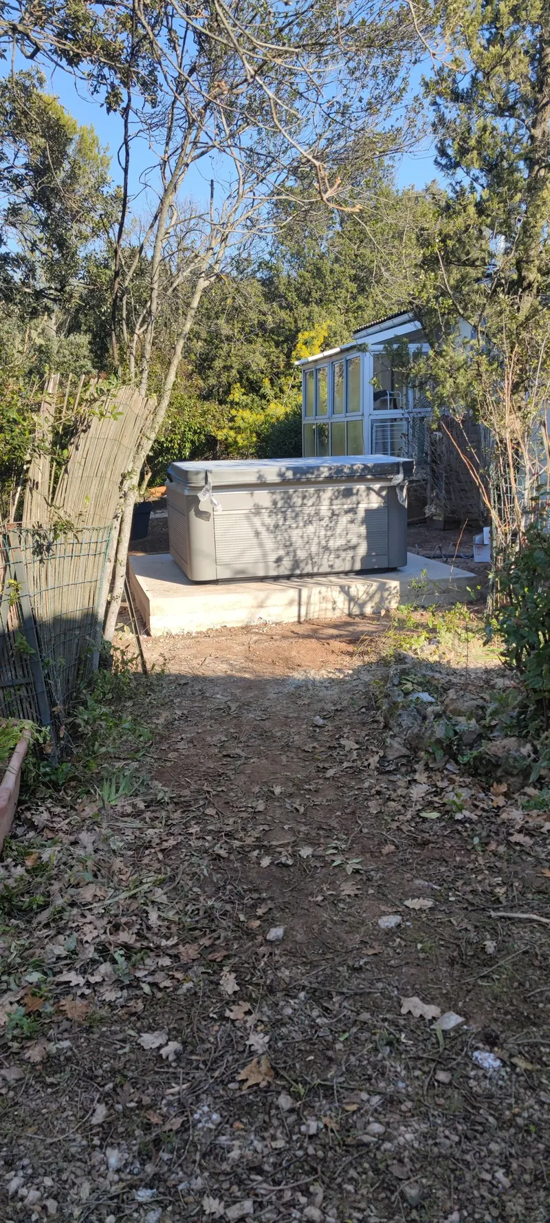 Spa couvert sur sa dalle au bout du chemin, petite véranda vitrée derrière