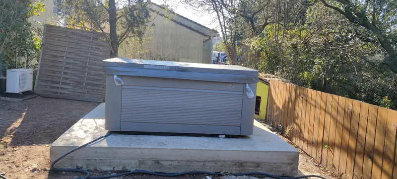 Spa couvert de face sur la dalle béton, palissade en bois, cabane jaune et climatisation