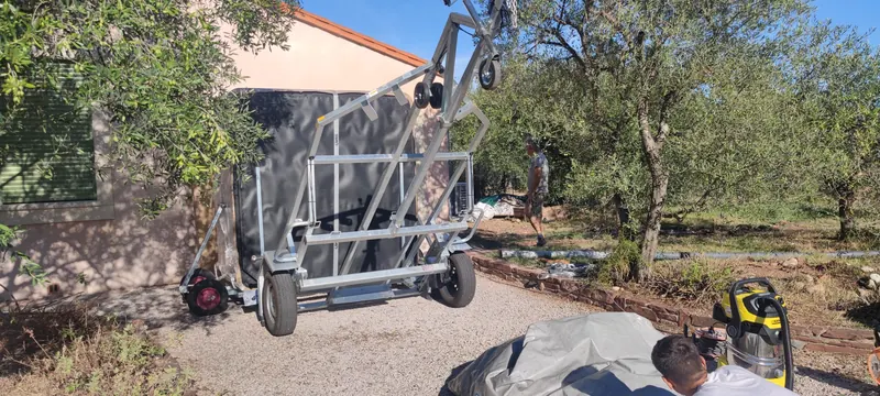 Spa debout sur un chariot de manutention, jardin d'oliviers, coussin gris et aspirateur jaune au premier plan