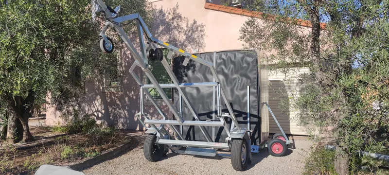 Chariot de manutention vu de côté, spa debout devant un volet roulant beige, allée de gravier