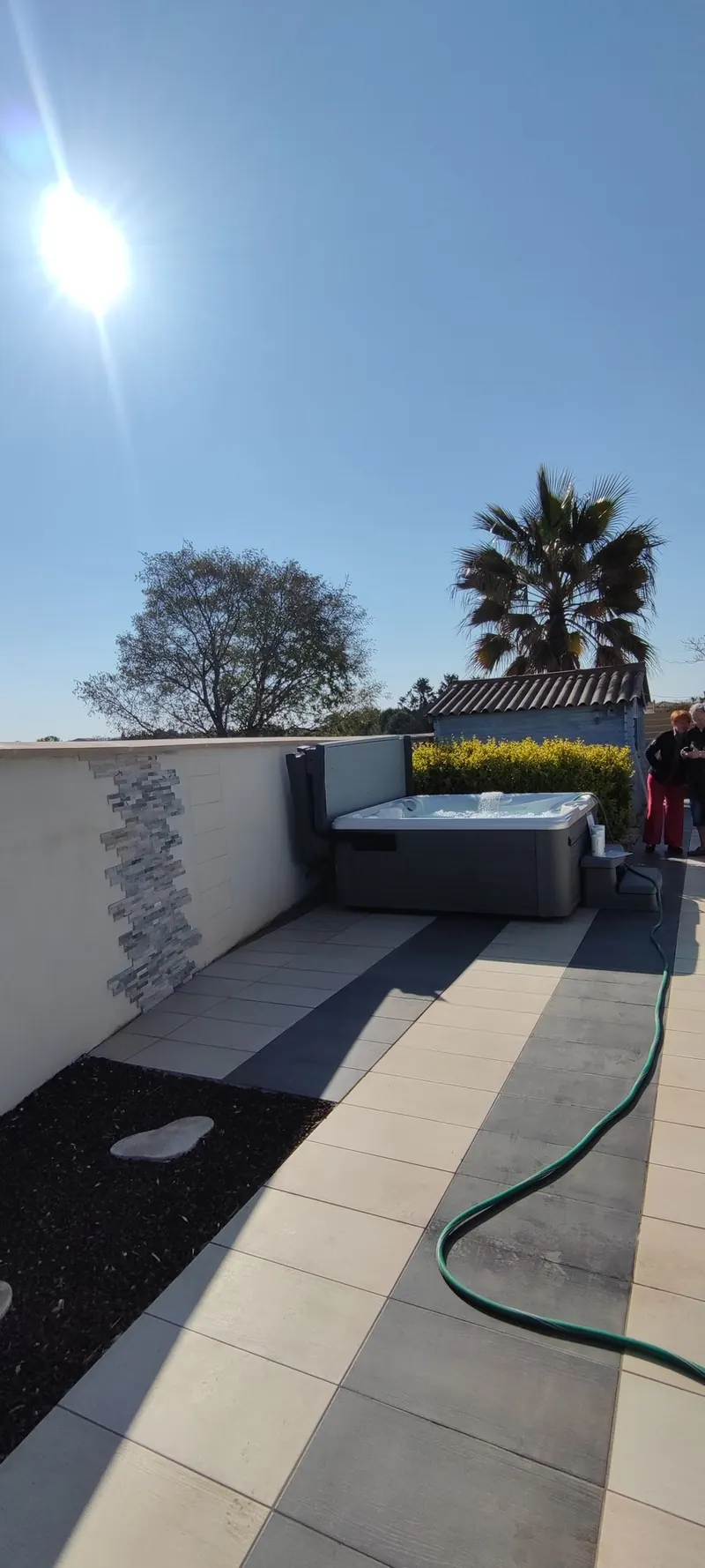 Spa encastré dans la terrasse pavée, mur de clôture blanc et pergola