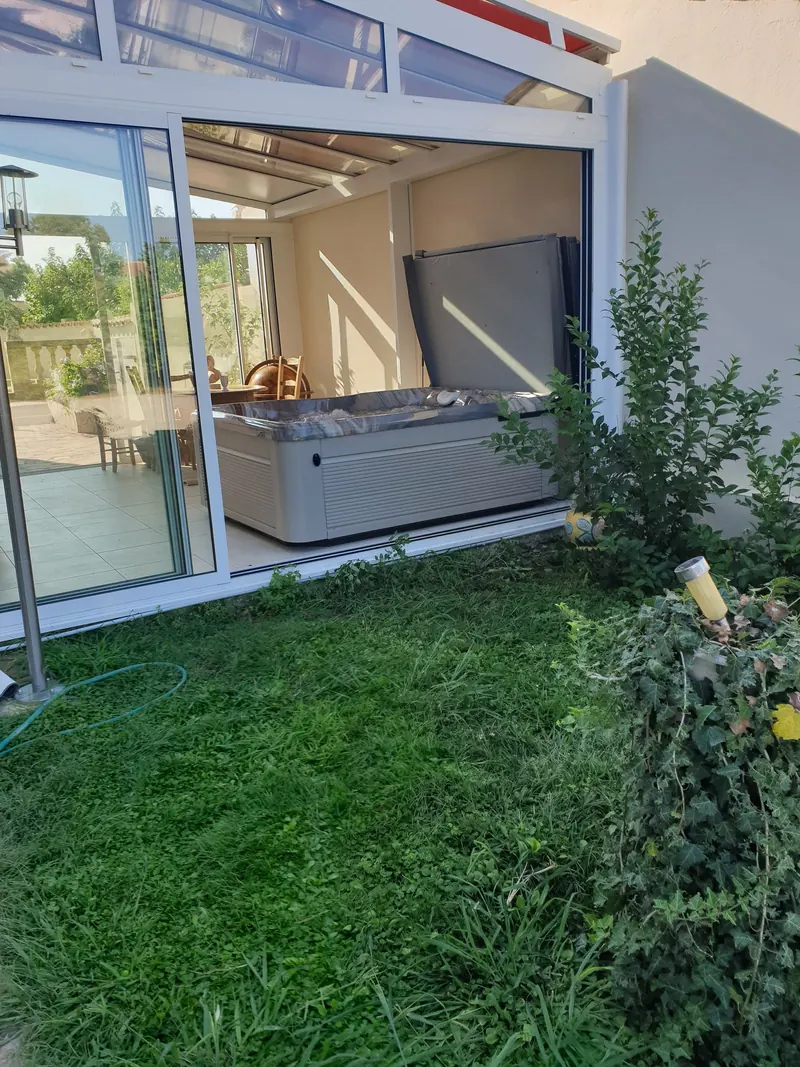 Spa dans une véranda vitrée dont les baies grandes ouvertes donnent sur le jardin