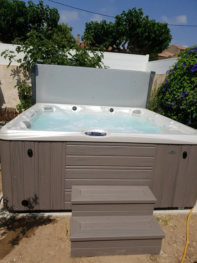 Spa en marche vu de face avec son marchepied gris, posé sur une dalle dans un jardin à Loupian