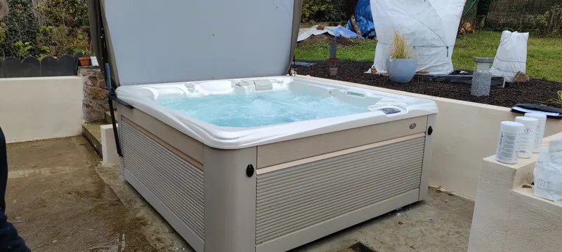 Spa blanc rempli d'eau turquoise, vu de face, sur sa dalle